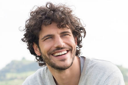 Smiling man with curly hair showcasing a bright, white smile, representing the benefits of professional teeth whitening services at Evolve Dental Care.